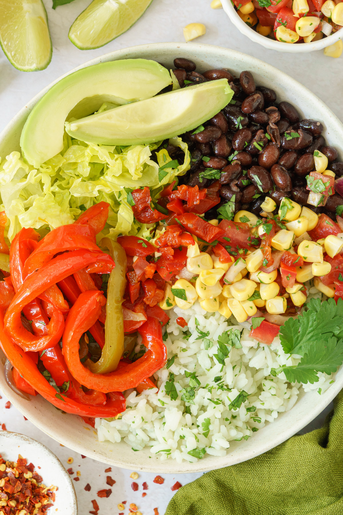 close up of a bowl with assembled cooked rice, black beans, corns, tender bell peppers, tomatoes, romaine leaves and avocado