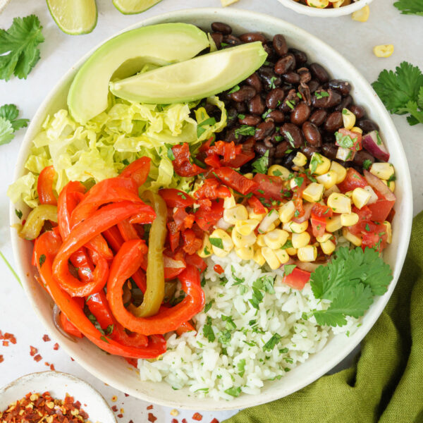 cropped image of a bowl with assembled cooked rice, black beans, corns, romaine leaves, cilantro leaves, tender bell peppers and avocado