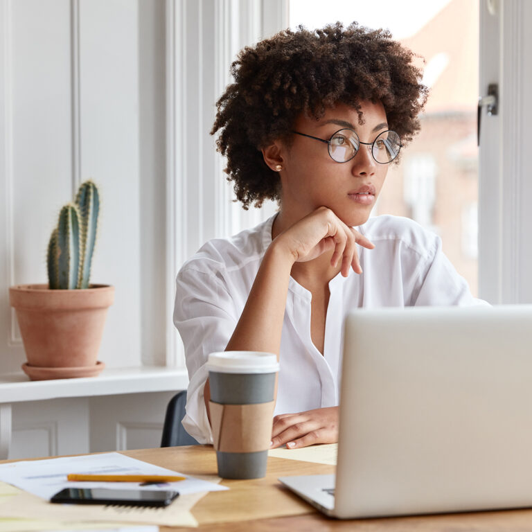 Woman sitting at her desk in front of her laptop looking away