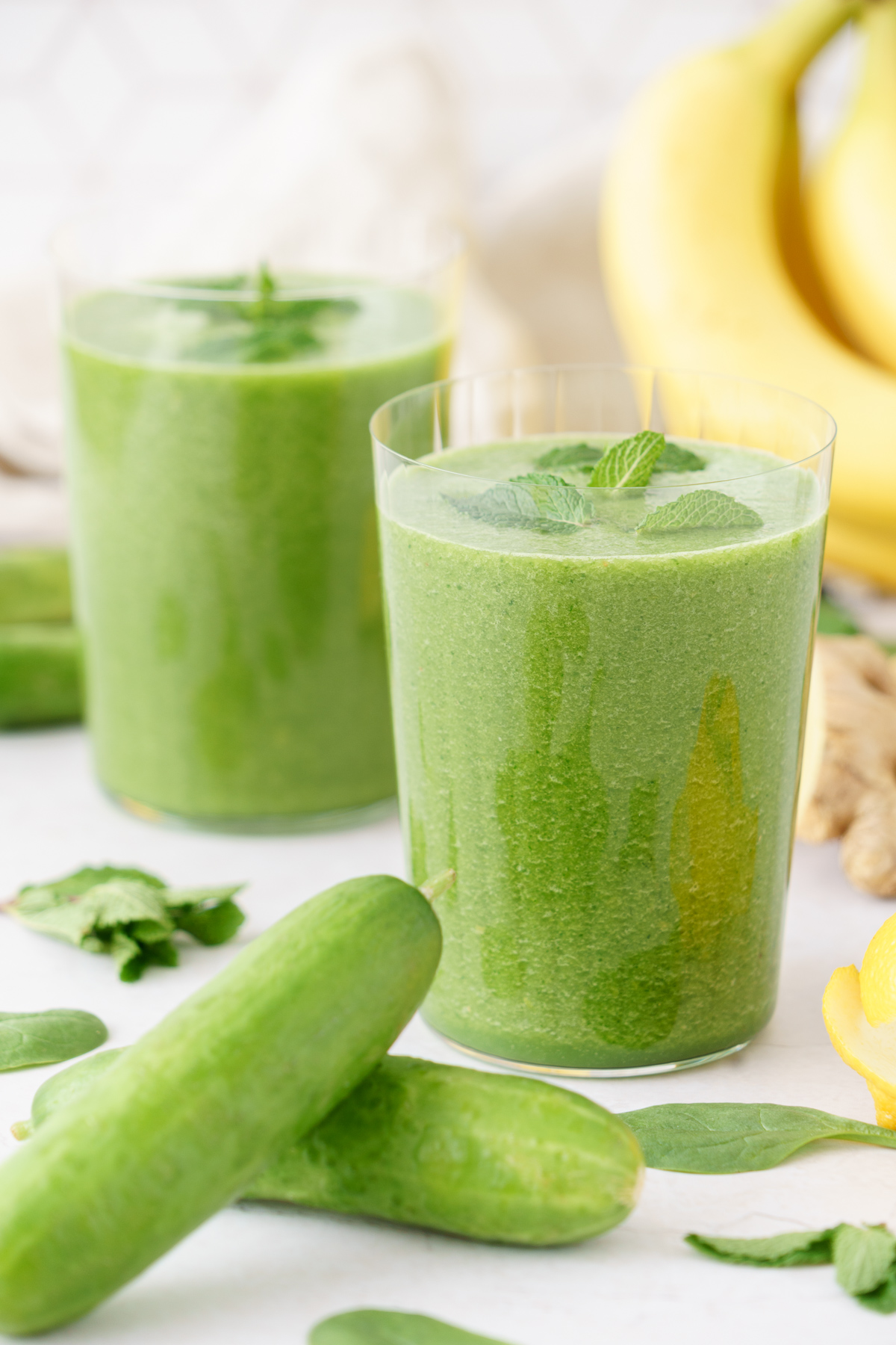 Two tall glasses full of green detox smoothie top with mint leaves.