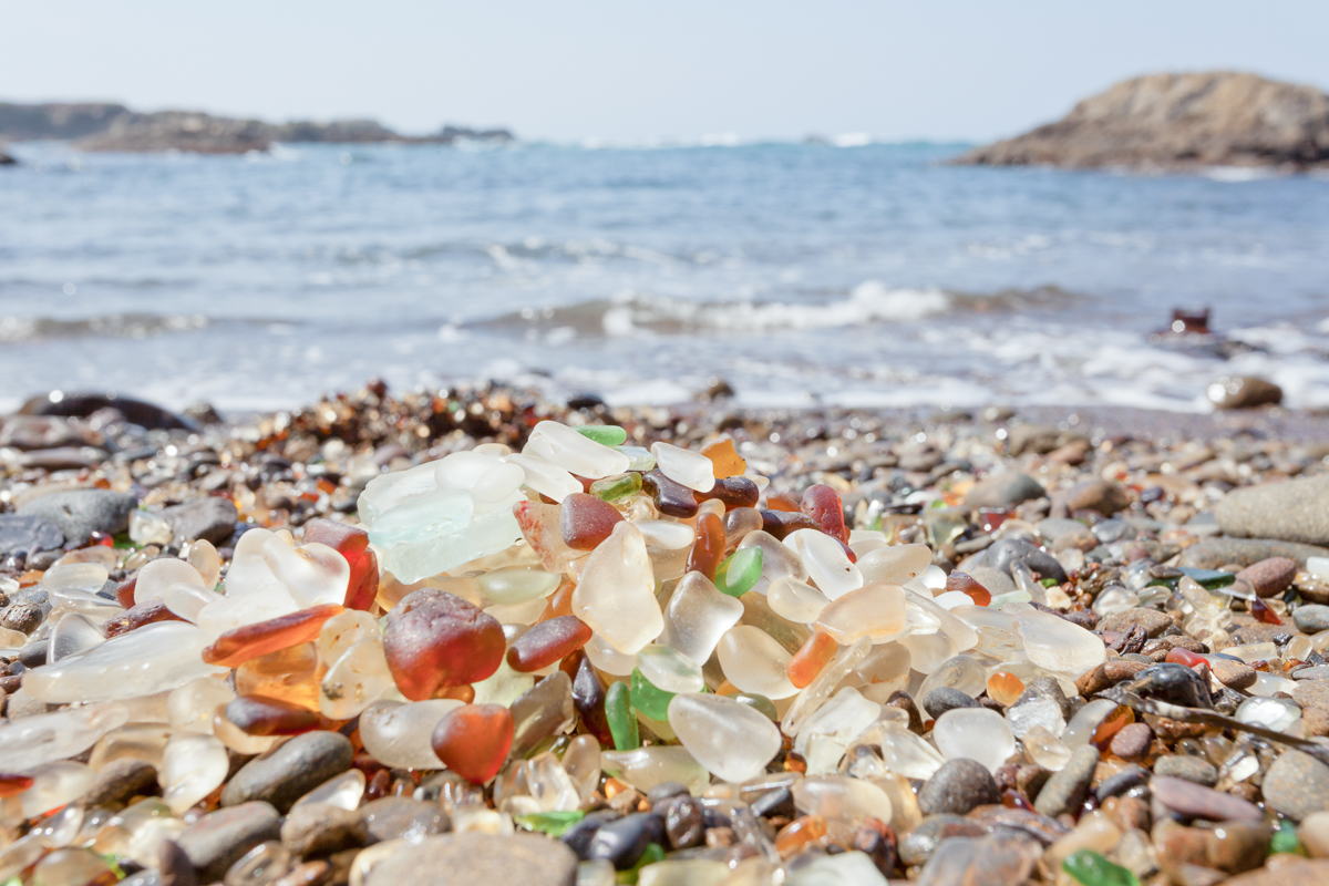 Pile of rounded glass shards or sea-glass of Fort Bragg, California, US with blurry Pacific Ocean background