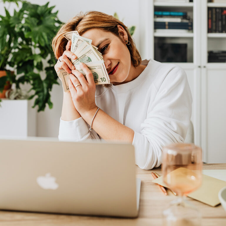 Woman holding cash in from of her laptop