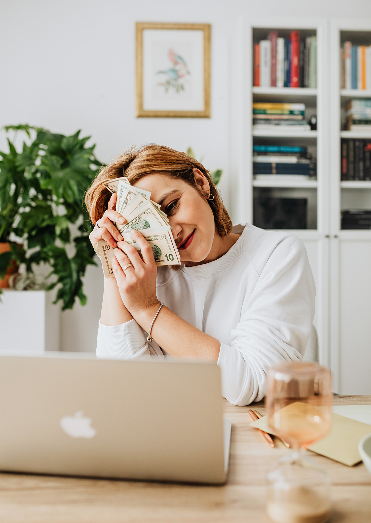 Woman holding cash in from of her laptop