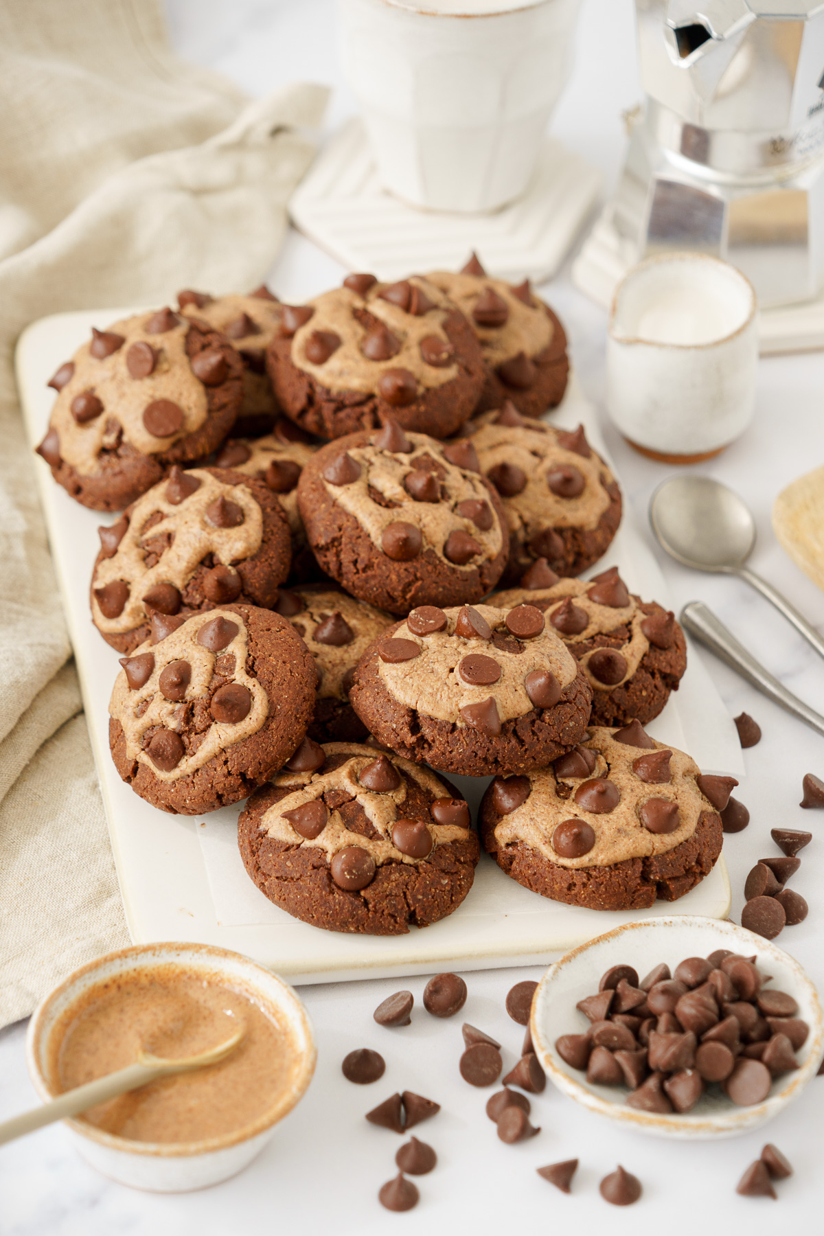 close-up view of a freshly baked batch of Chocolate Chickpea Flour Cookies with scattered chocolate chips, accompanied by a bowl filled with a mixture of cookie toppings