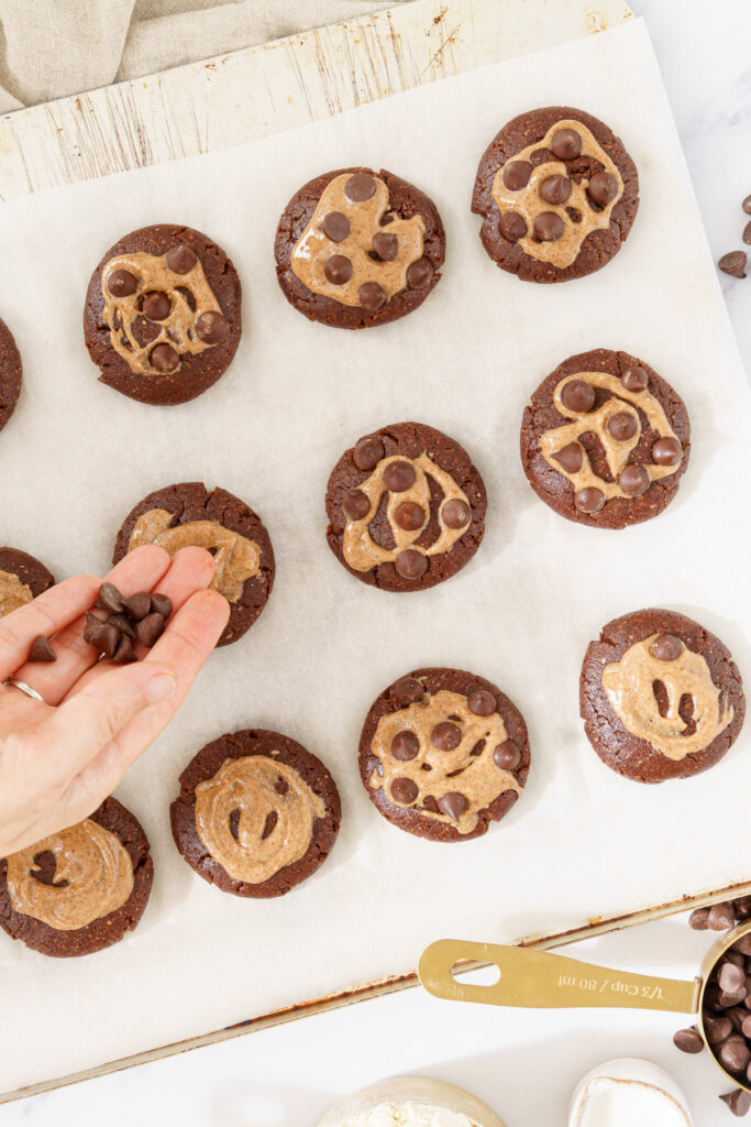 overhead view of a hand sprinkling chocolate chips onto a cookie dough, preparing it for baking