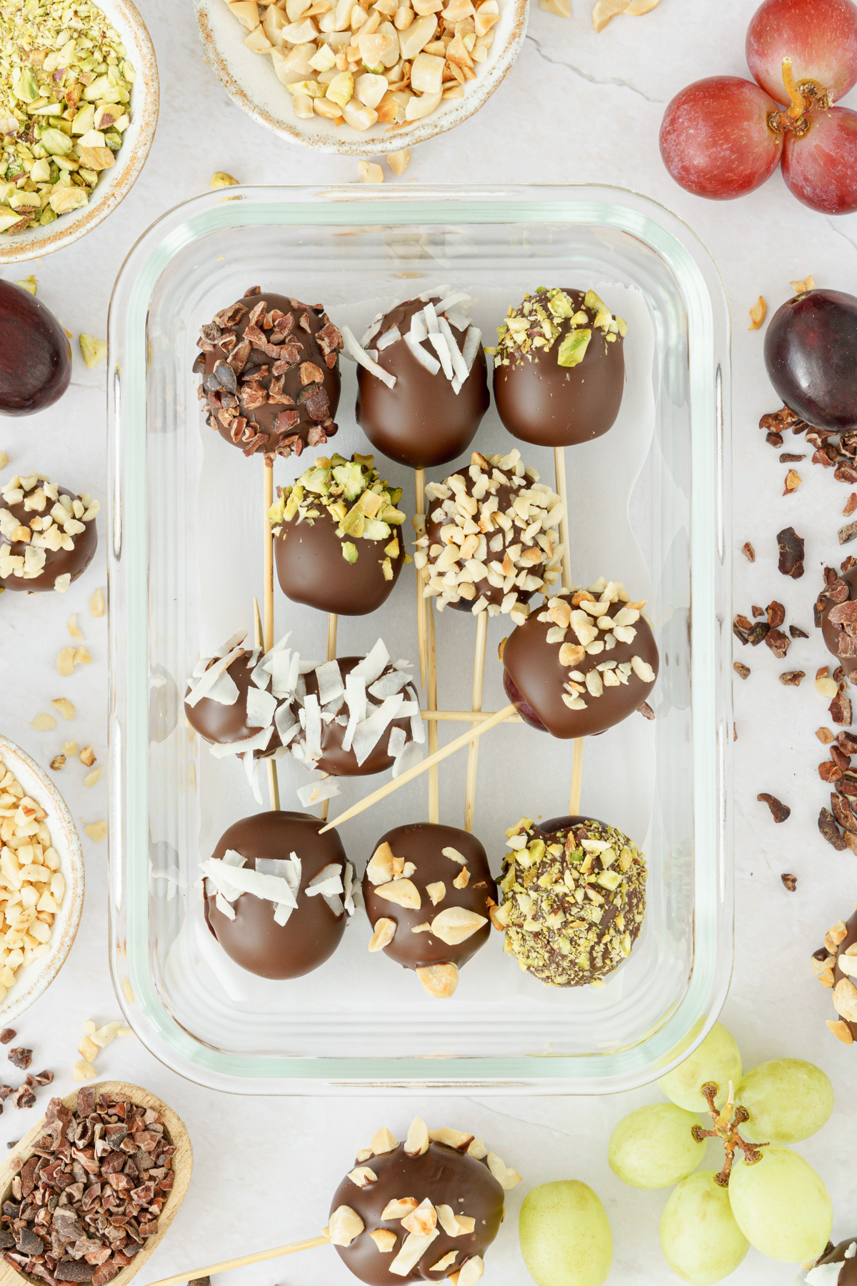 Glass container with chocolate-covered grapes with various toppings ready for storage.