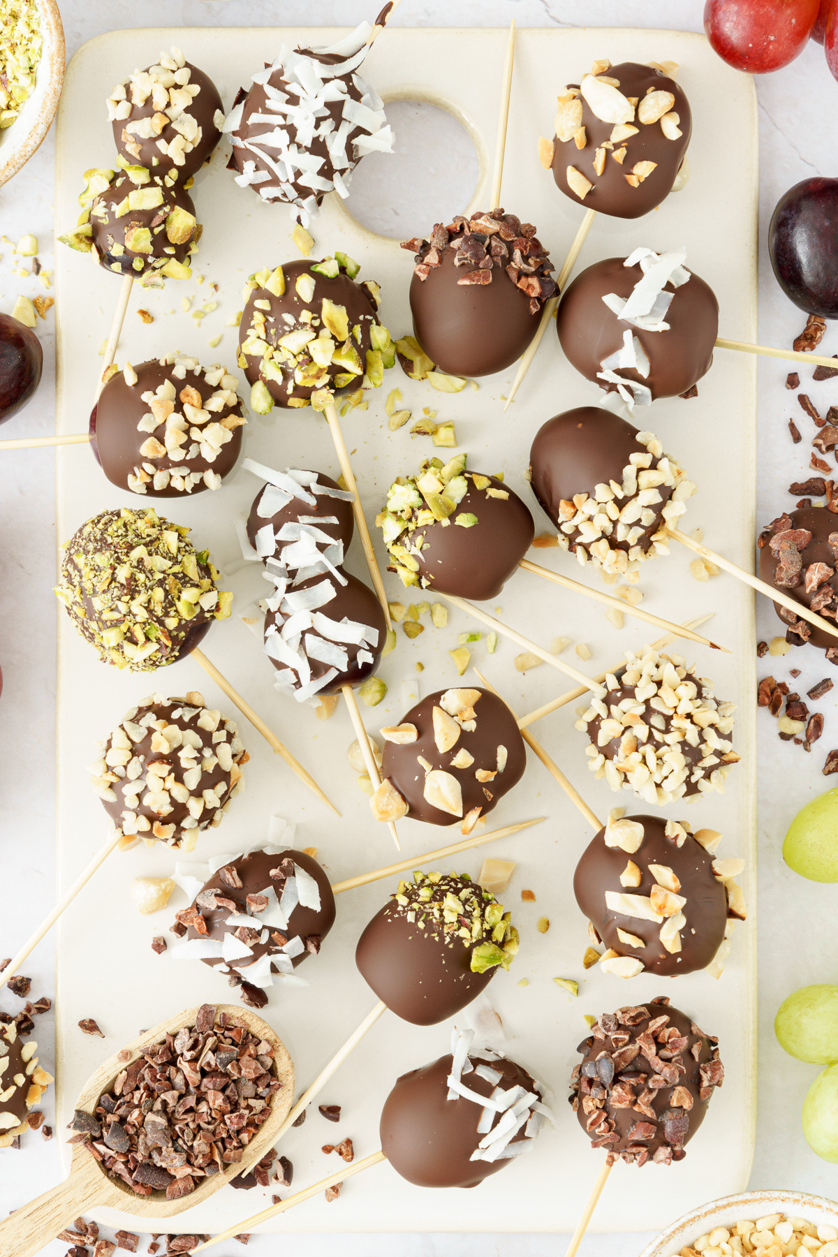 Skewers with chocolate-covered grapes, garnished with nuts, shredded coconut, and crushed chocolate.