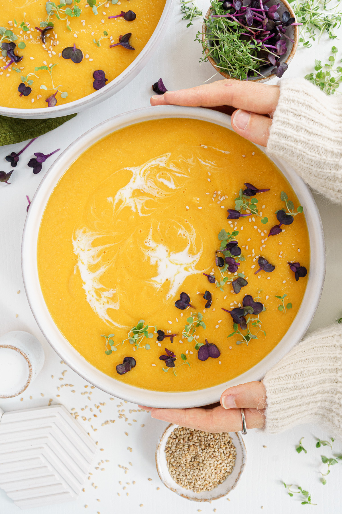 Hands holding onto a bowl of vegan carrot ginger soup.