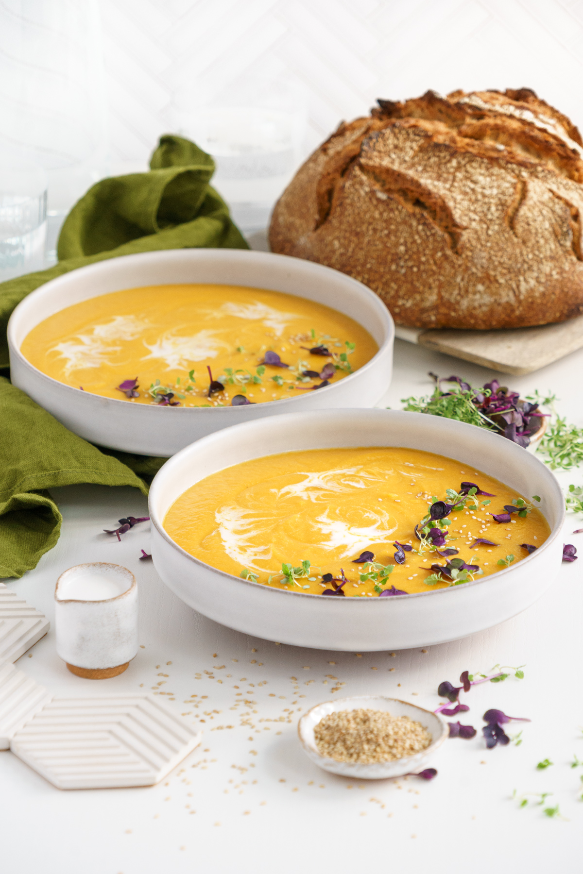 Two bowls of carrot ginger soup served on the table with a loaf of crusty bread.