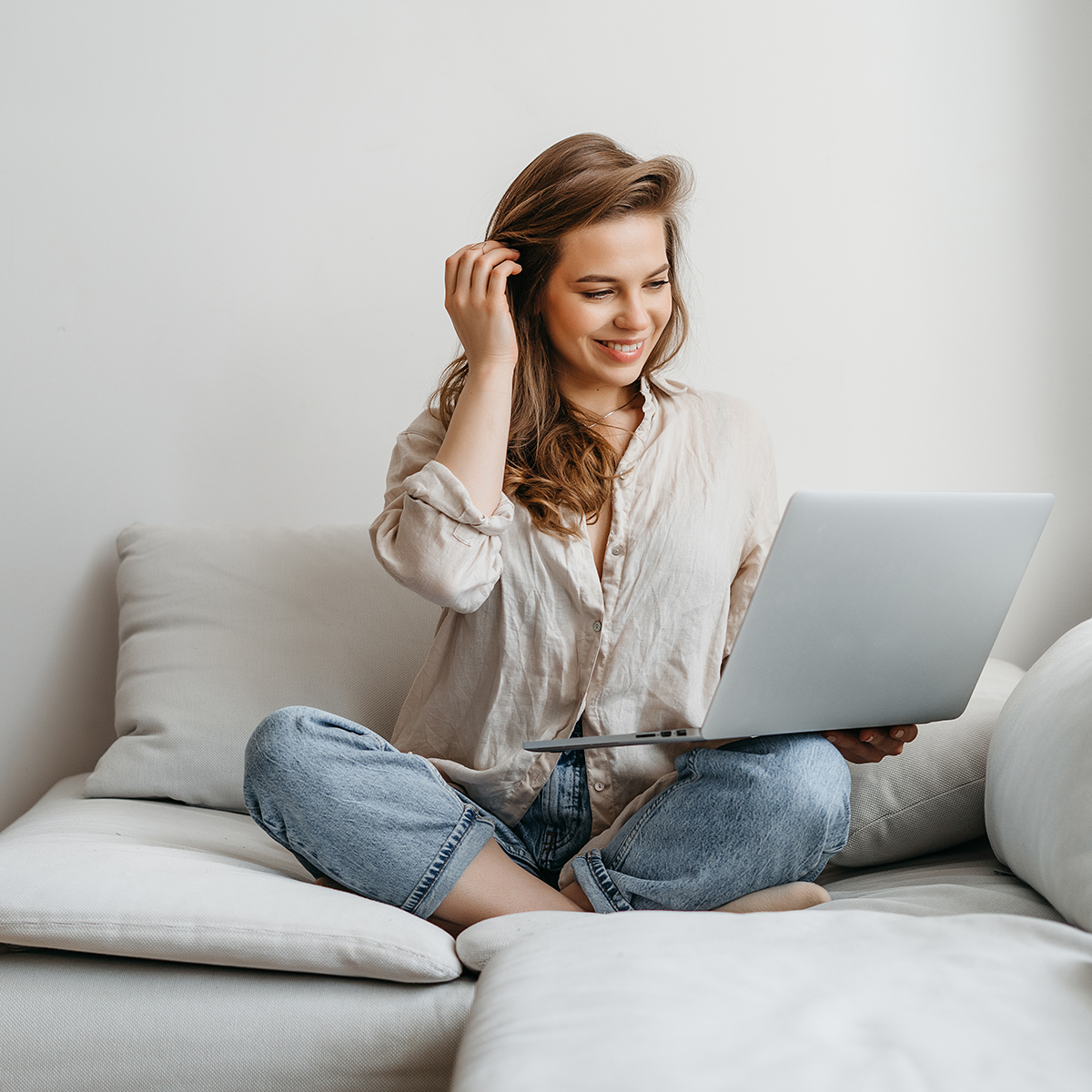 Woman sitting on a grey sofa smiling, working on her laptop.