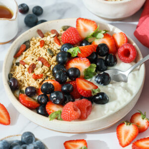 Bowl containing a mix of cottage cheese, fresh strawberries, blueberries, raspberries, and granola.