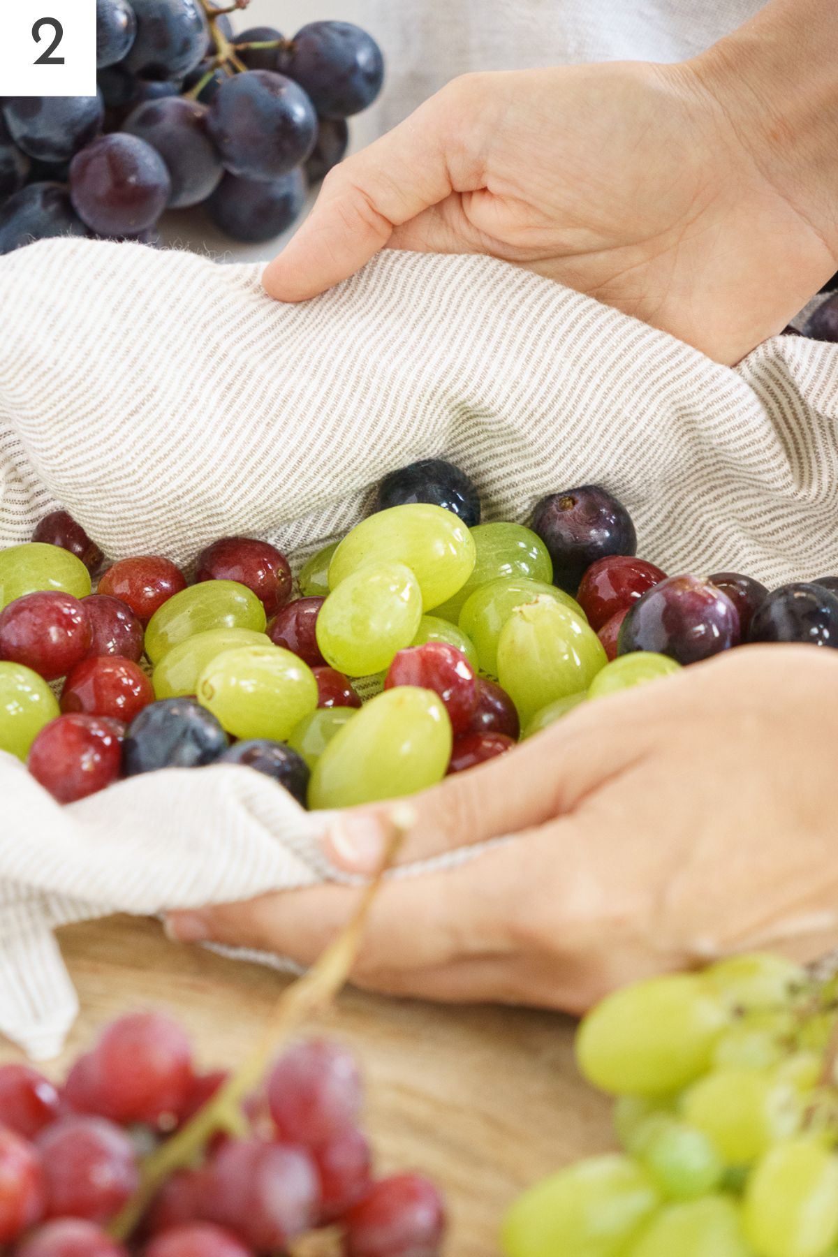 Hands patting dry freshly washed grapes with a kitchen towel.