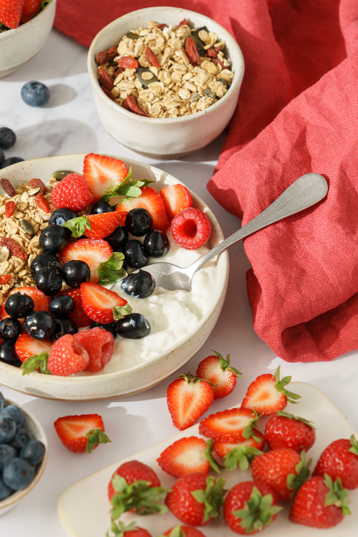 Bowl filled with cottage cheese topped with granola and mixed berries with a spoon inserted in the cottage cheese.