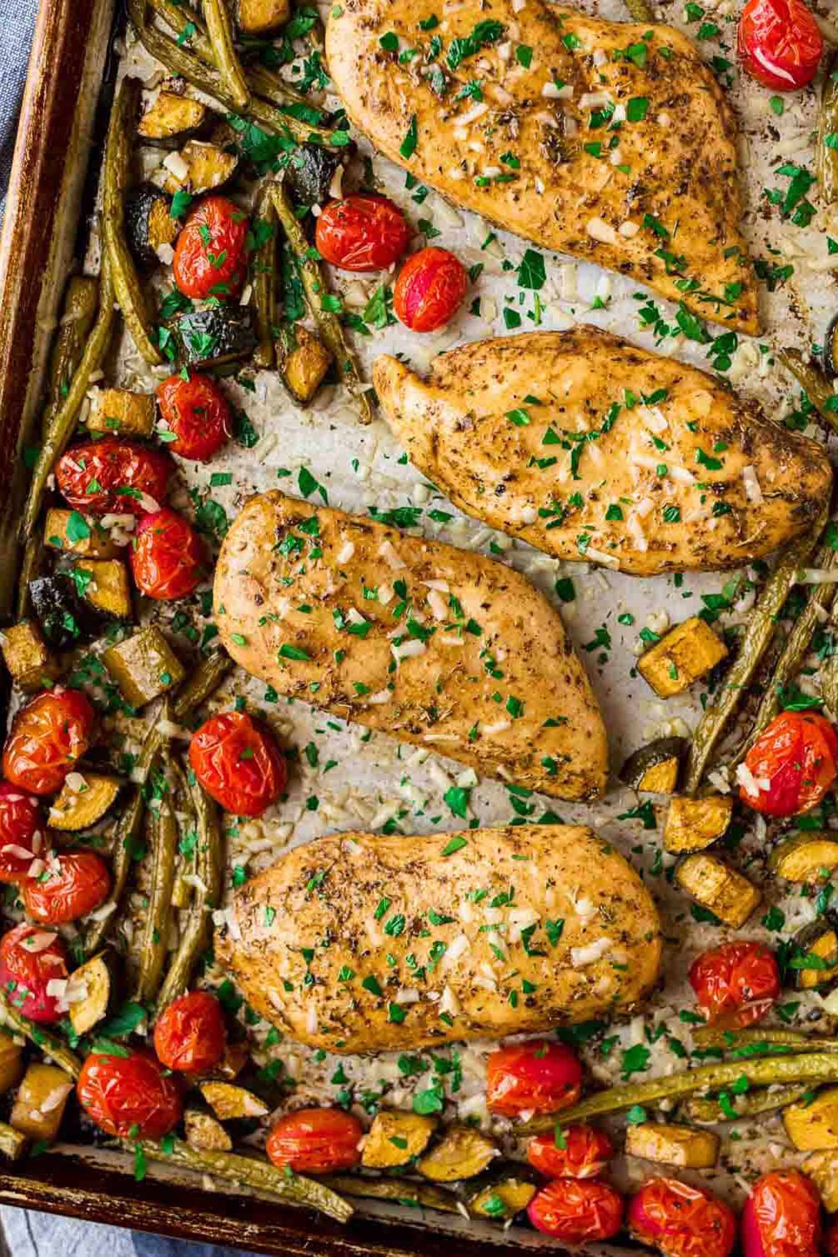 Baked chicken with cherry tomatoes and beans on a baking sheet.