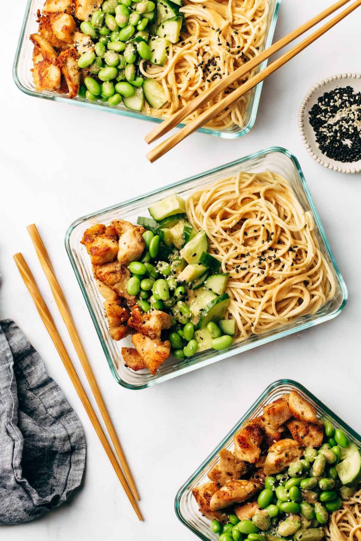 Sesame noodle bowls with noodles, chicken, edamame in meal prep containers.