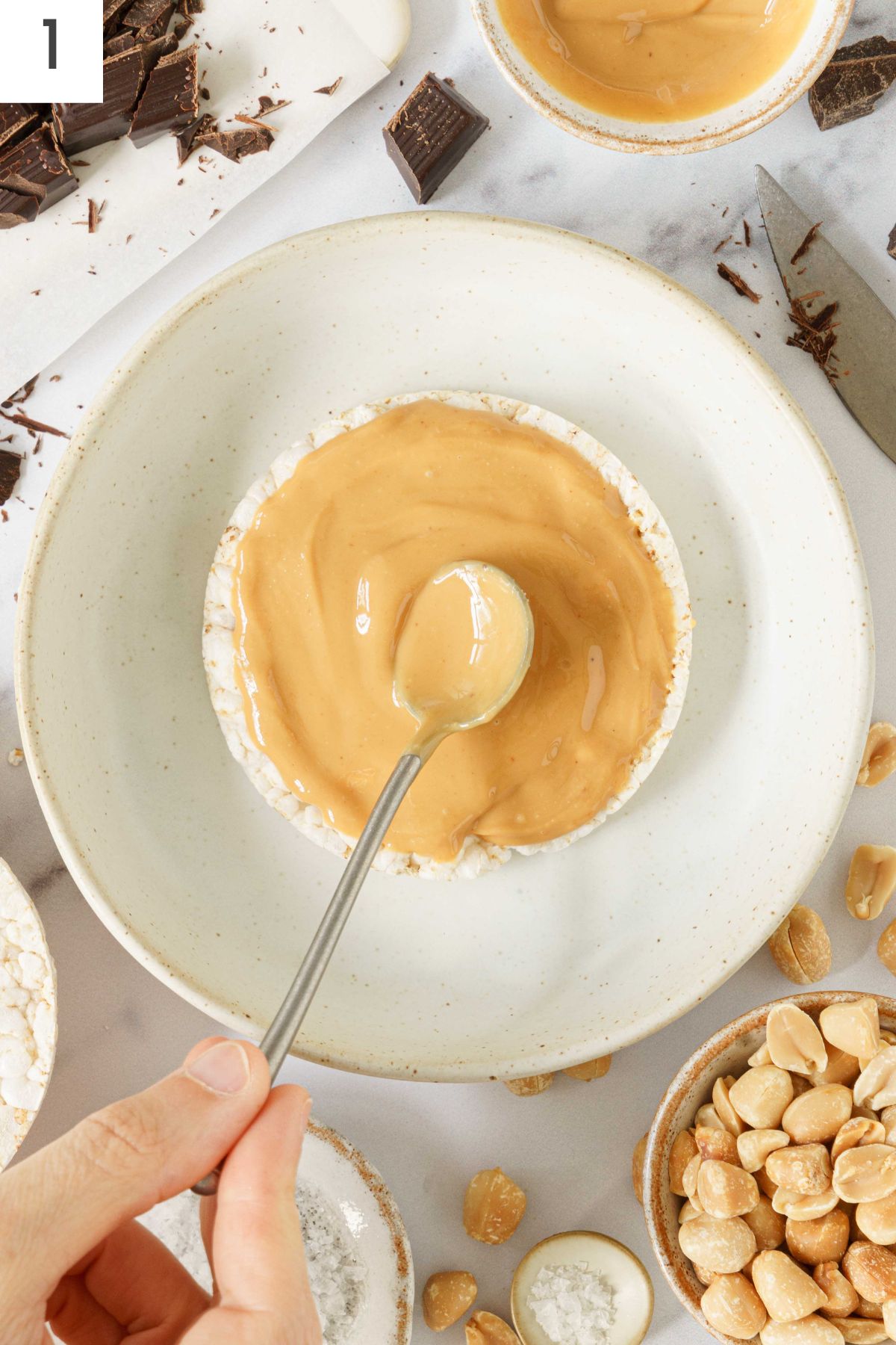 Hand spreading peanut butter on a rice cake with a spoon.