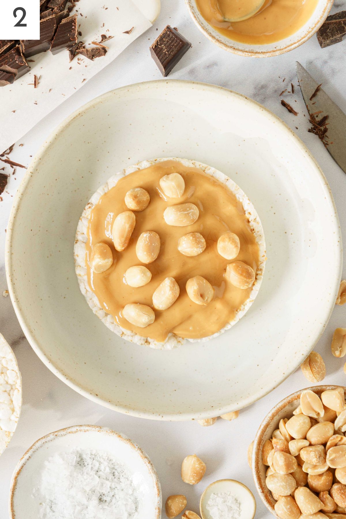 Roasted peanuts laid on a rice cake on top of peanut butter.