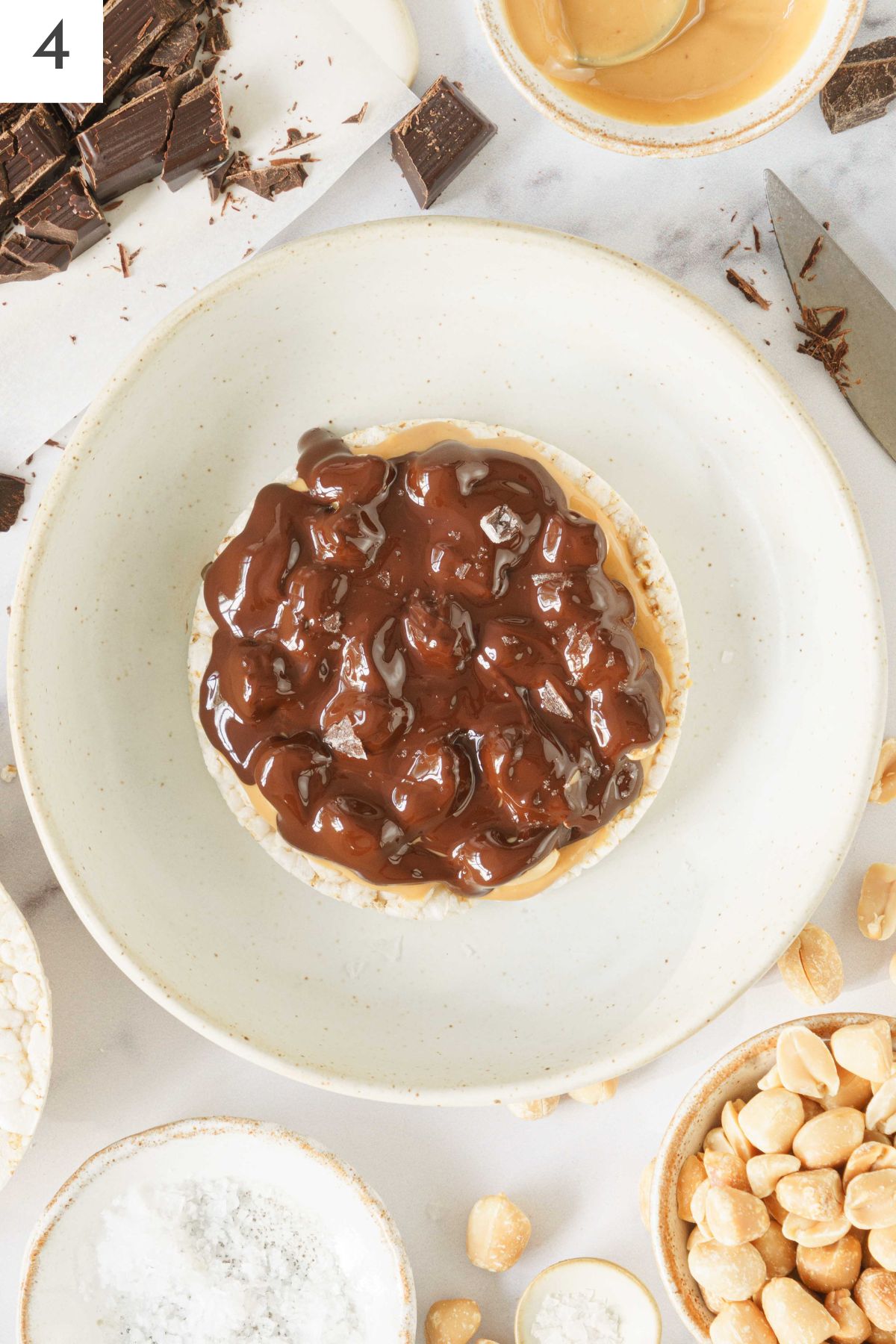 Hand spreading melted chocolate on top of the peanuts and peanut butter.