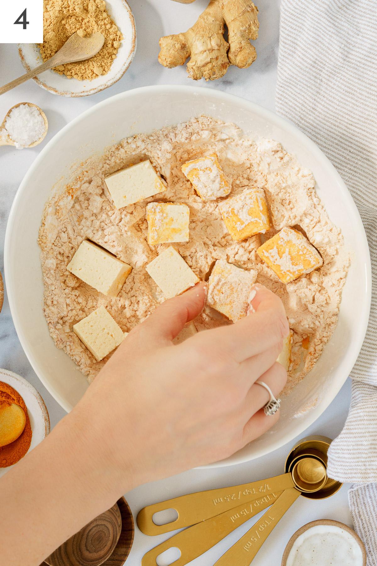 A hand coating the cube tofu with the coating mixture.