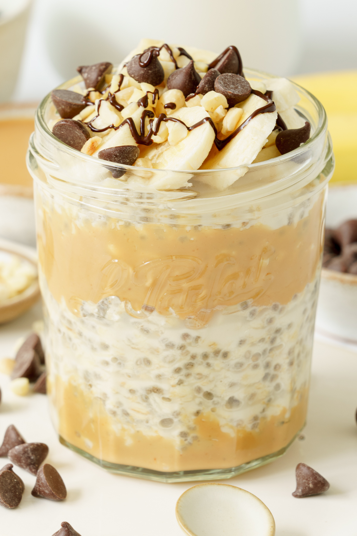 A jar of overnight oats with water topped with chocolate chips, peanut butter and banana.