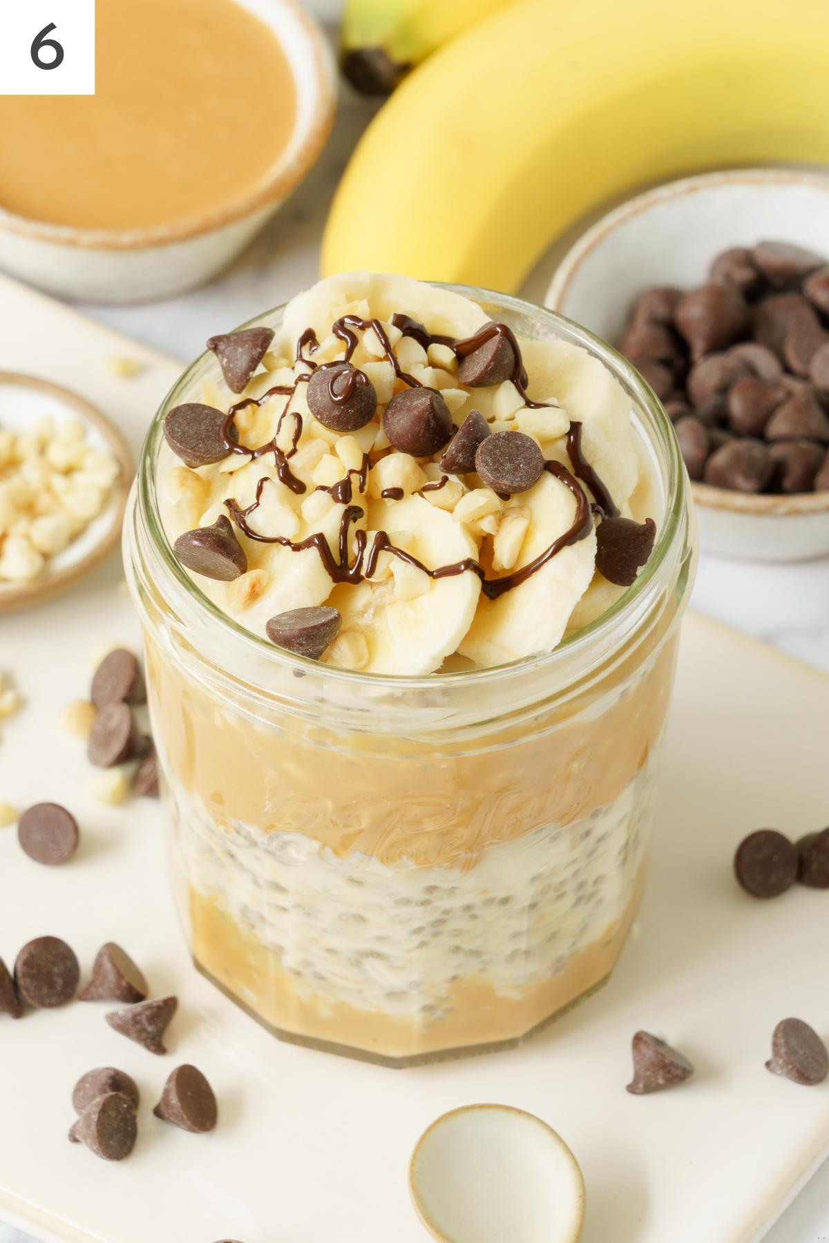 A jar of overnight oats topped with chocolate chips, peanut butter and banana.