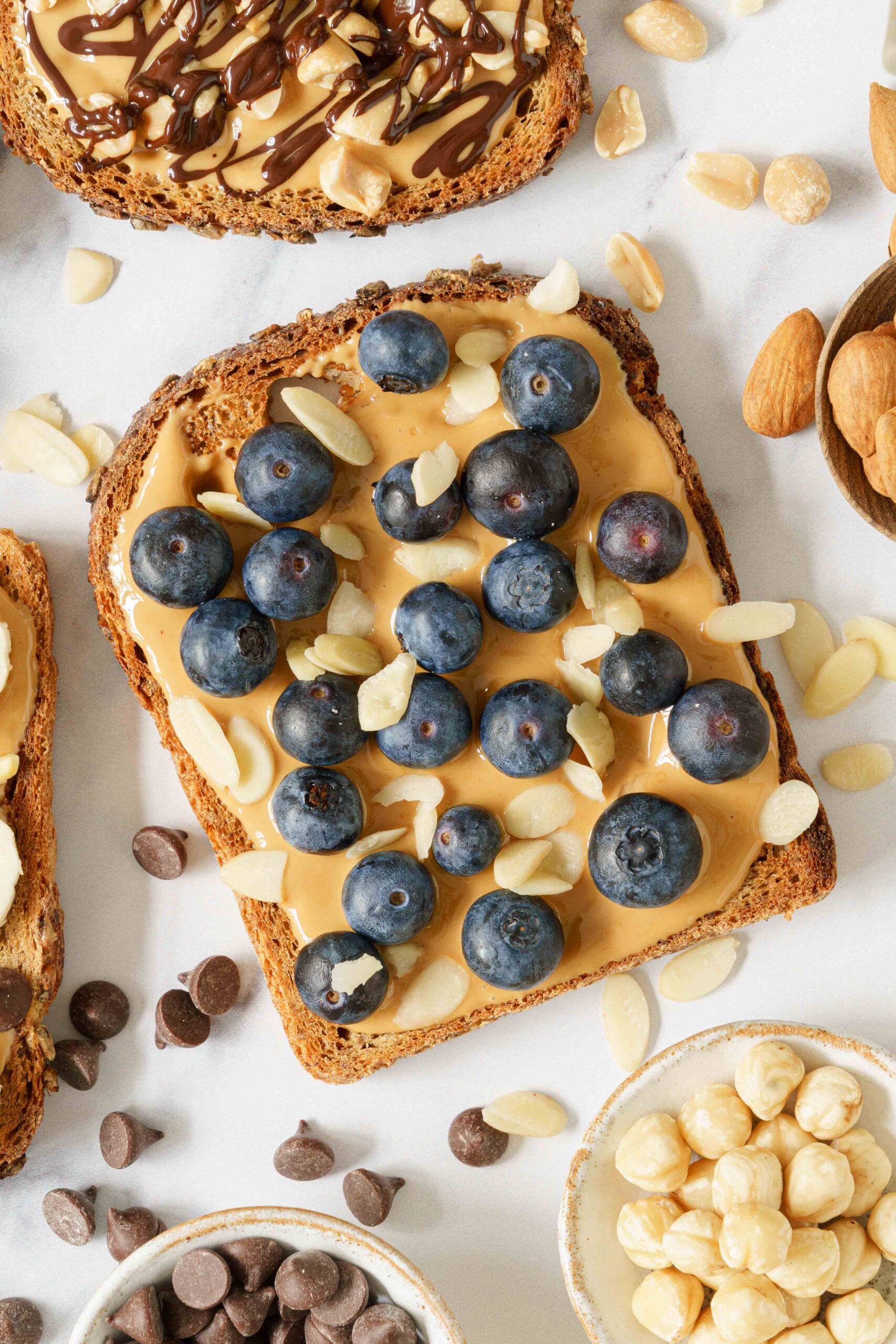 One slice of bread spread with peanut butter and topped with blueberries and almonds.