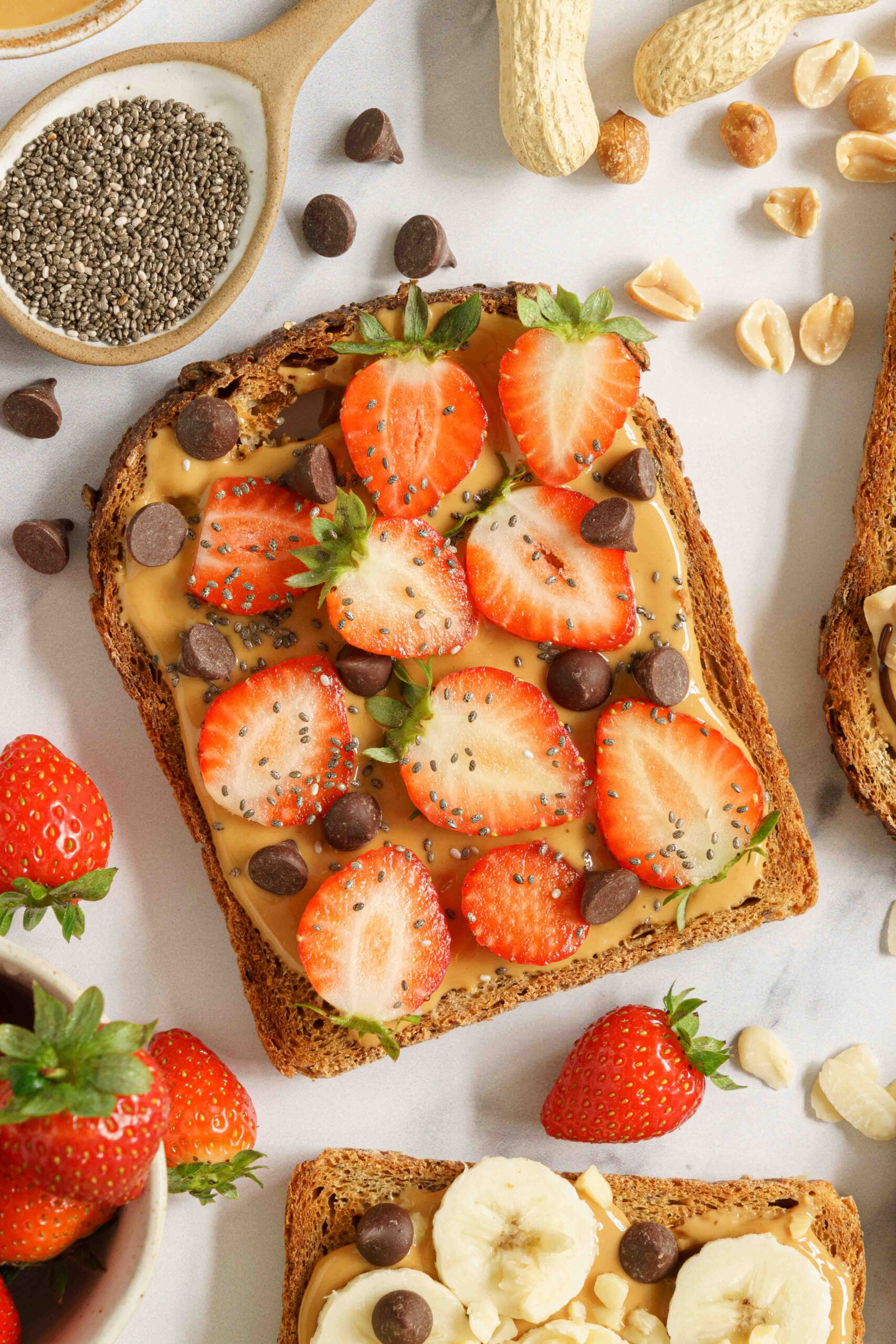 A single slice of bread spread with peanut butter, topped with slice of strawberries, chia seeds, and chocolate nibs.