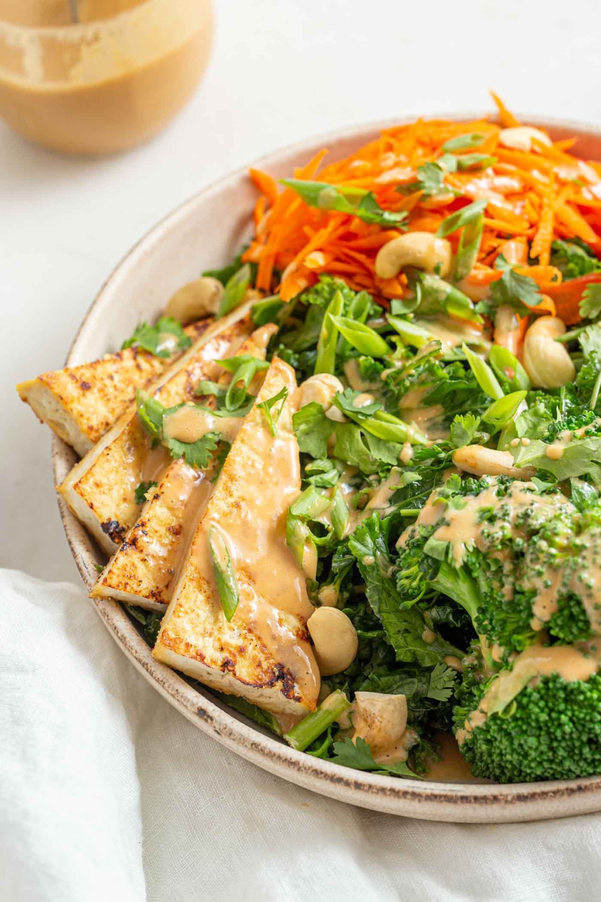 Tofu kale salad in a plate drizzled with peanut dressing.