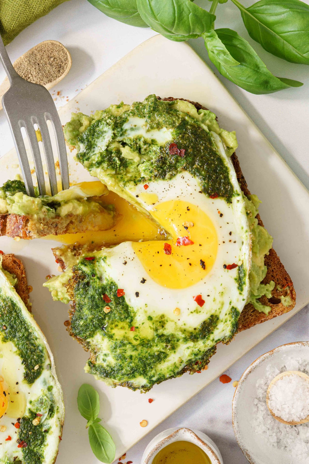 A fork cut a portion of the bread with pesto egg.