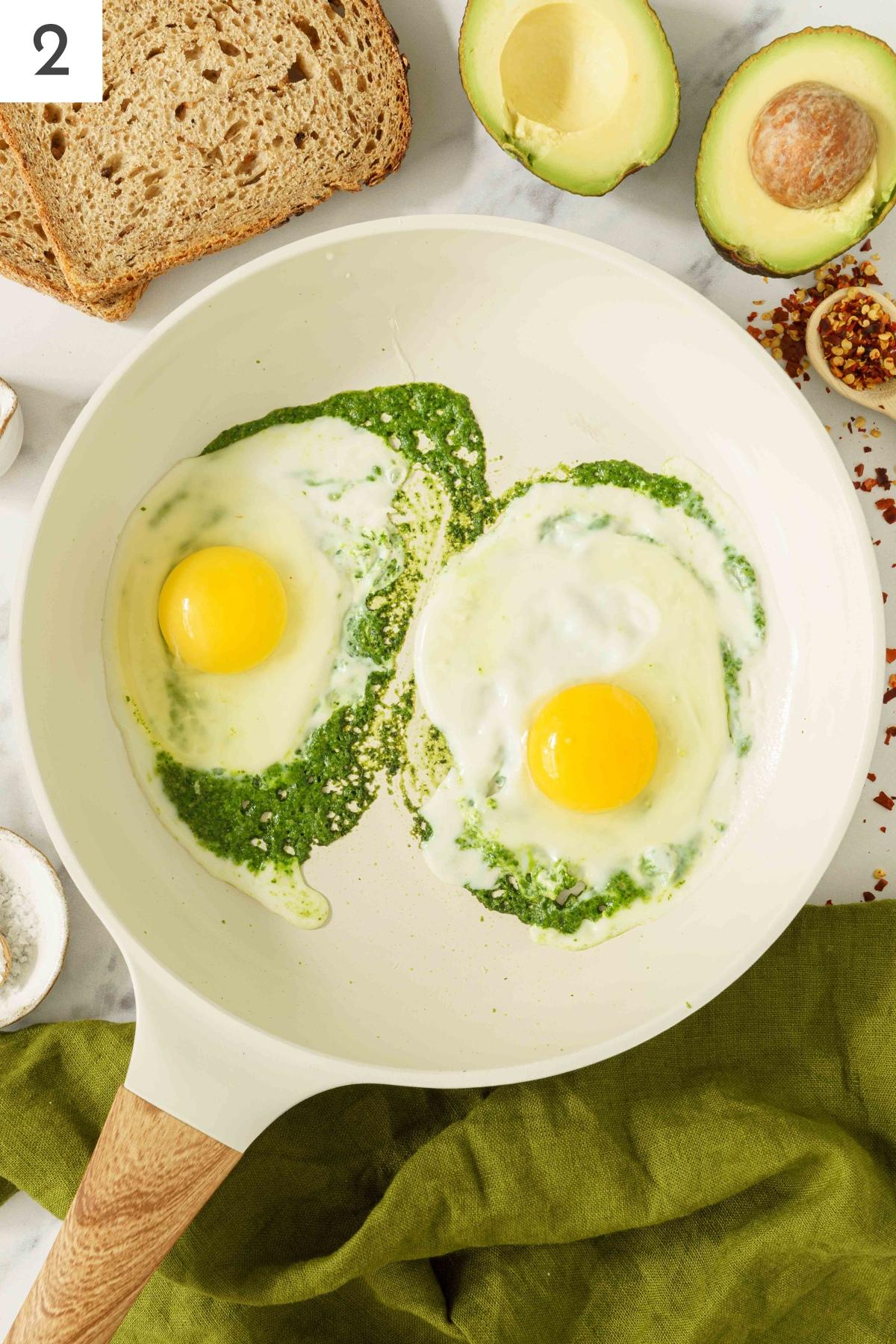 A pan with spreaded pesto and eggs