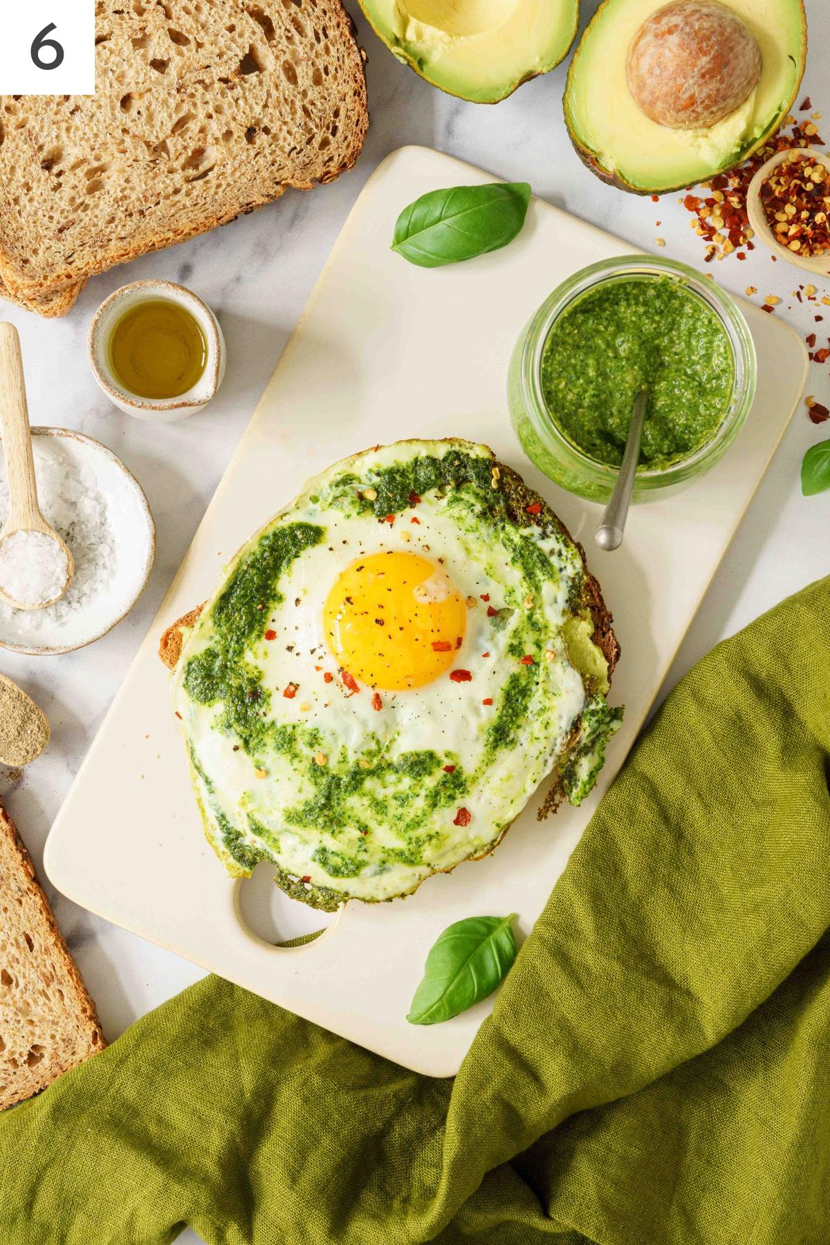 A slice of bread with mashed avocado topped with pesto egg.
