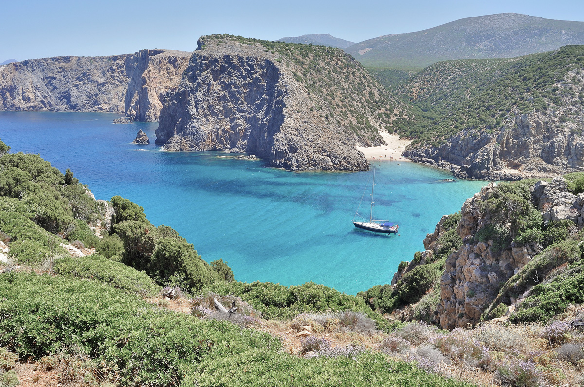 Aerial view of cala Domestica with azure water surrounded by mountains.