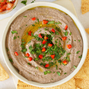 Black bean hummus on a round plate topped with fresh herbs and olive oil on top.