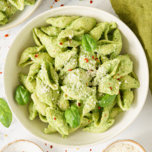Broccoli pesto pasta on a round plate topped with parmesan and chili flakes.