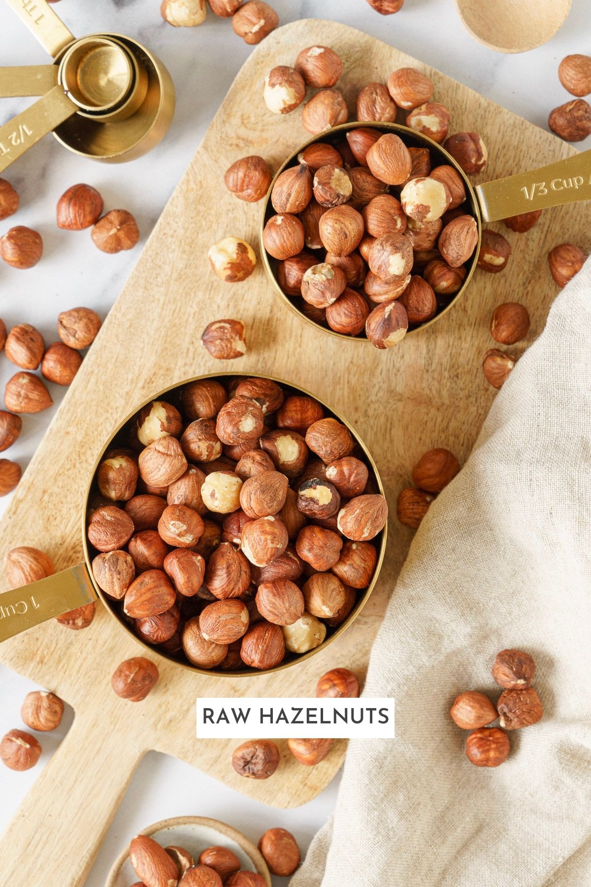 Two cups of raw hazelnuts on top of a chopping board.