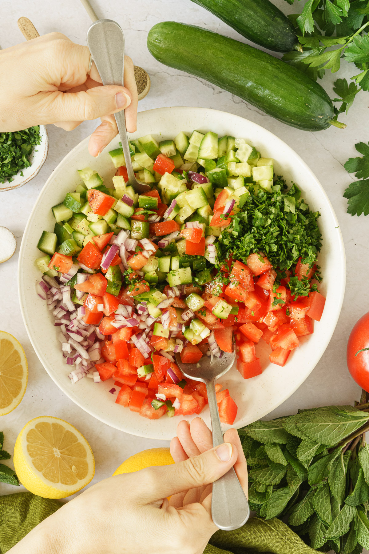 Hands tossing the middle eastern salad using a spoon.