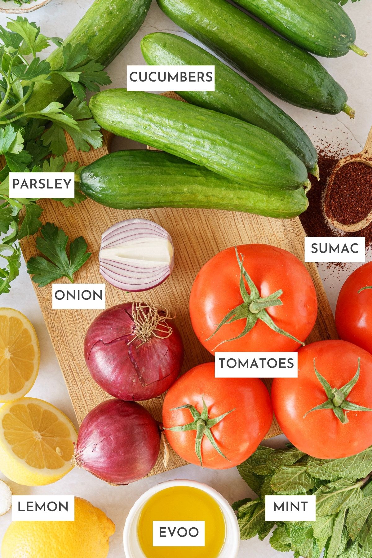Laid out ingredients of middle eastern salad: cucumbers, parsley, sumac, onion, tomatoes, lemon, evoo, and mint.