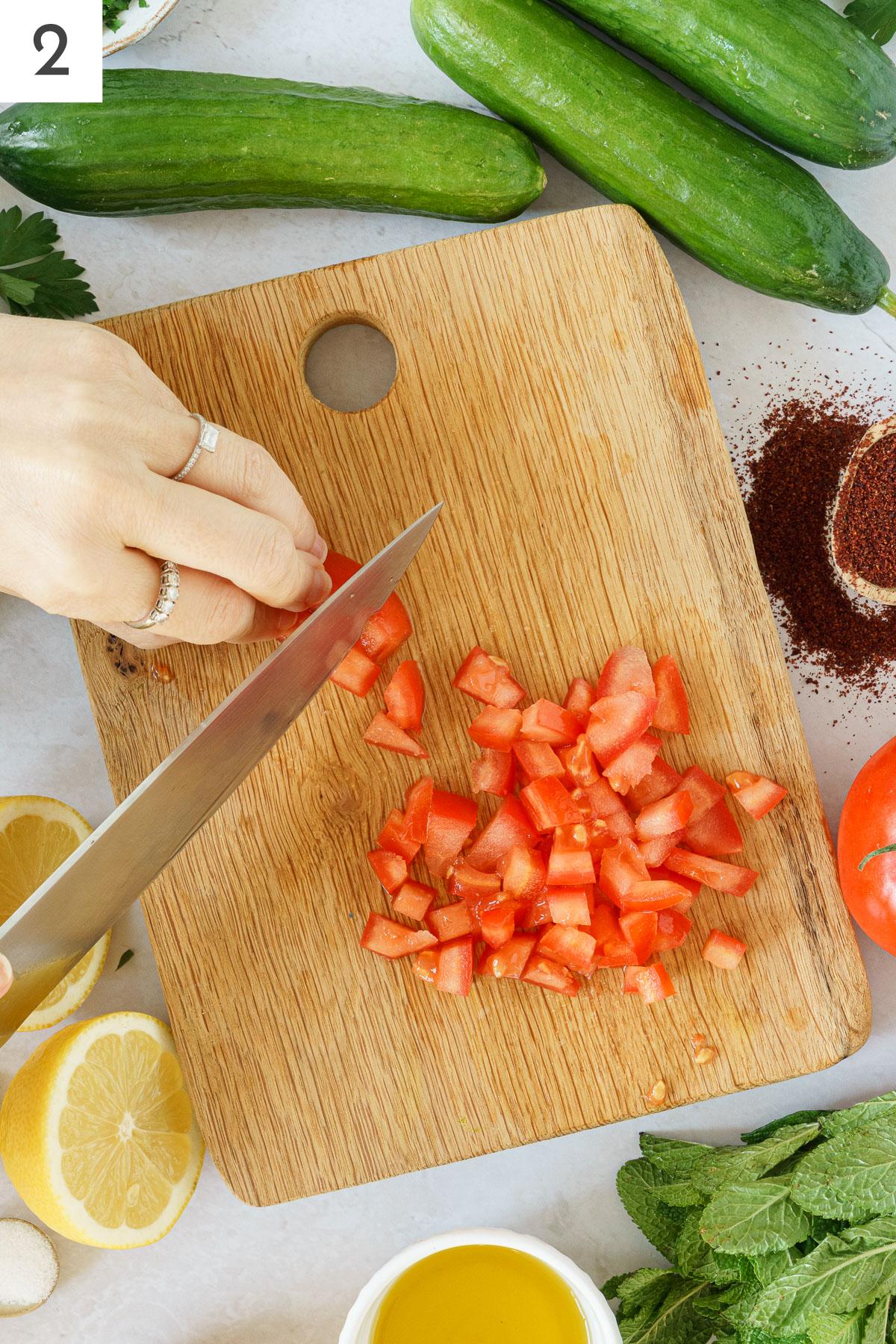 A hand chopping tomato on a cutting board.
