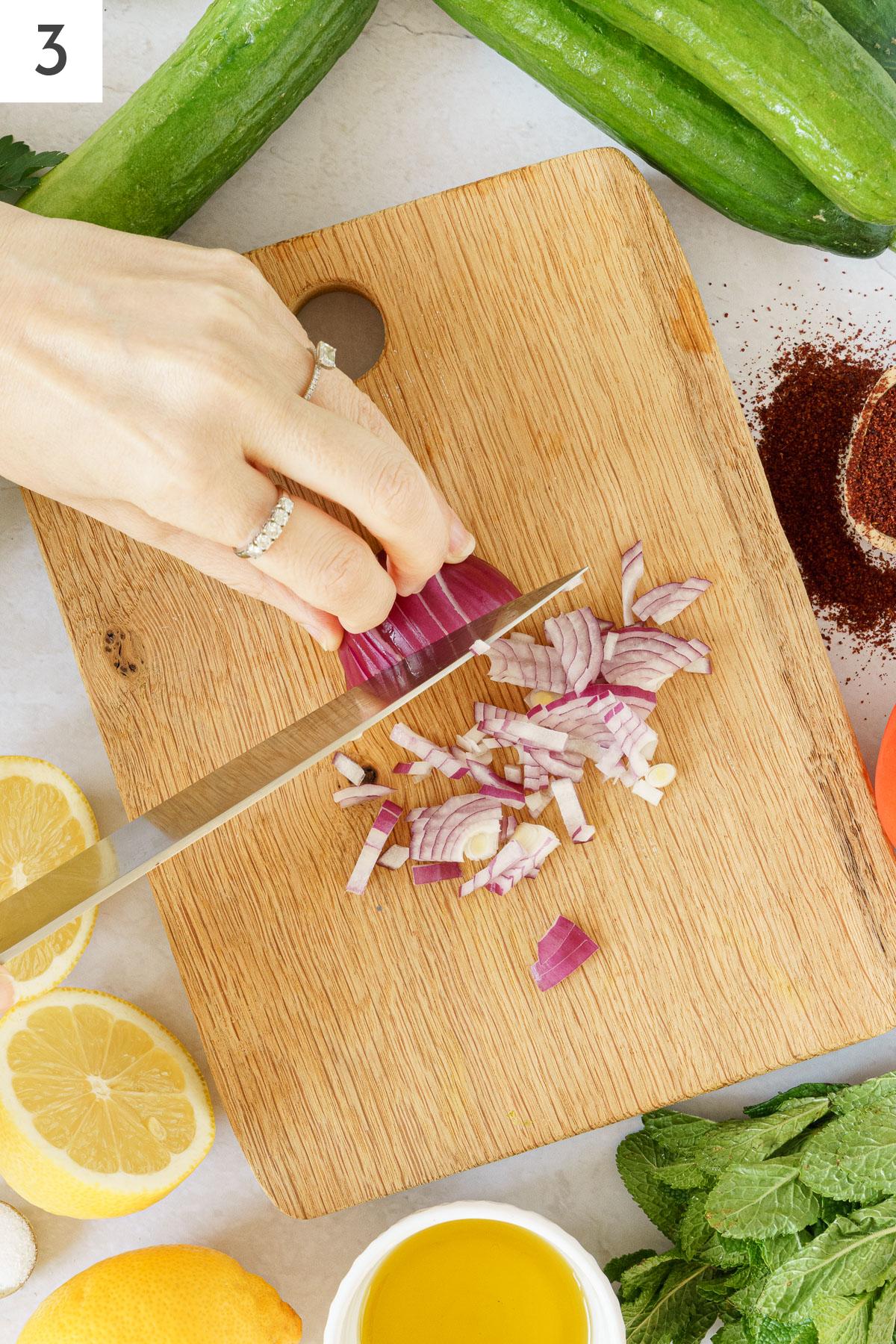 A hand chopping onion on a cutting board.
