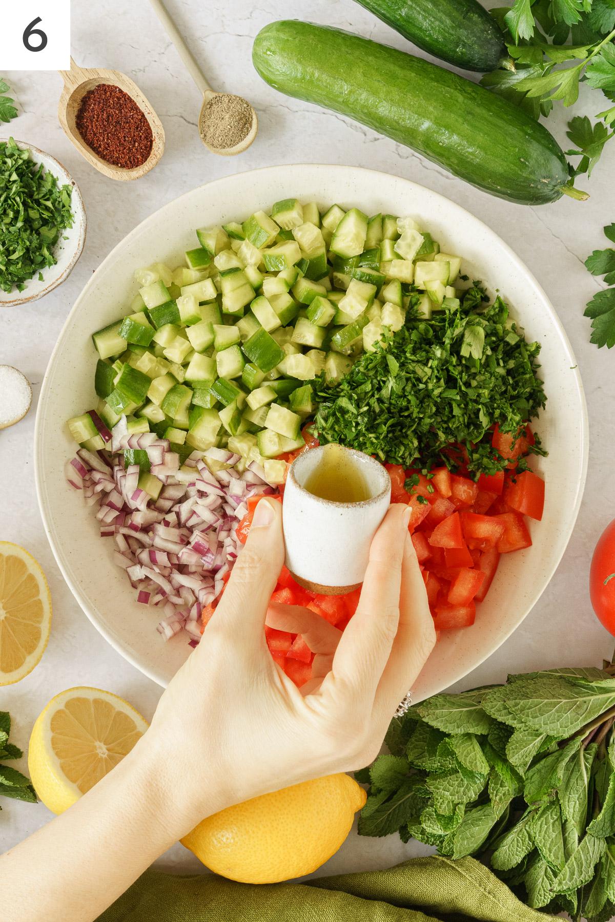 A hand pouring an olive oil in a bowl with chopped ingredients of middle eastern salad.