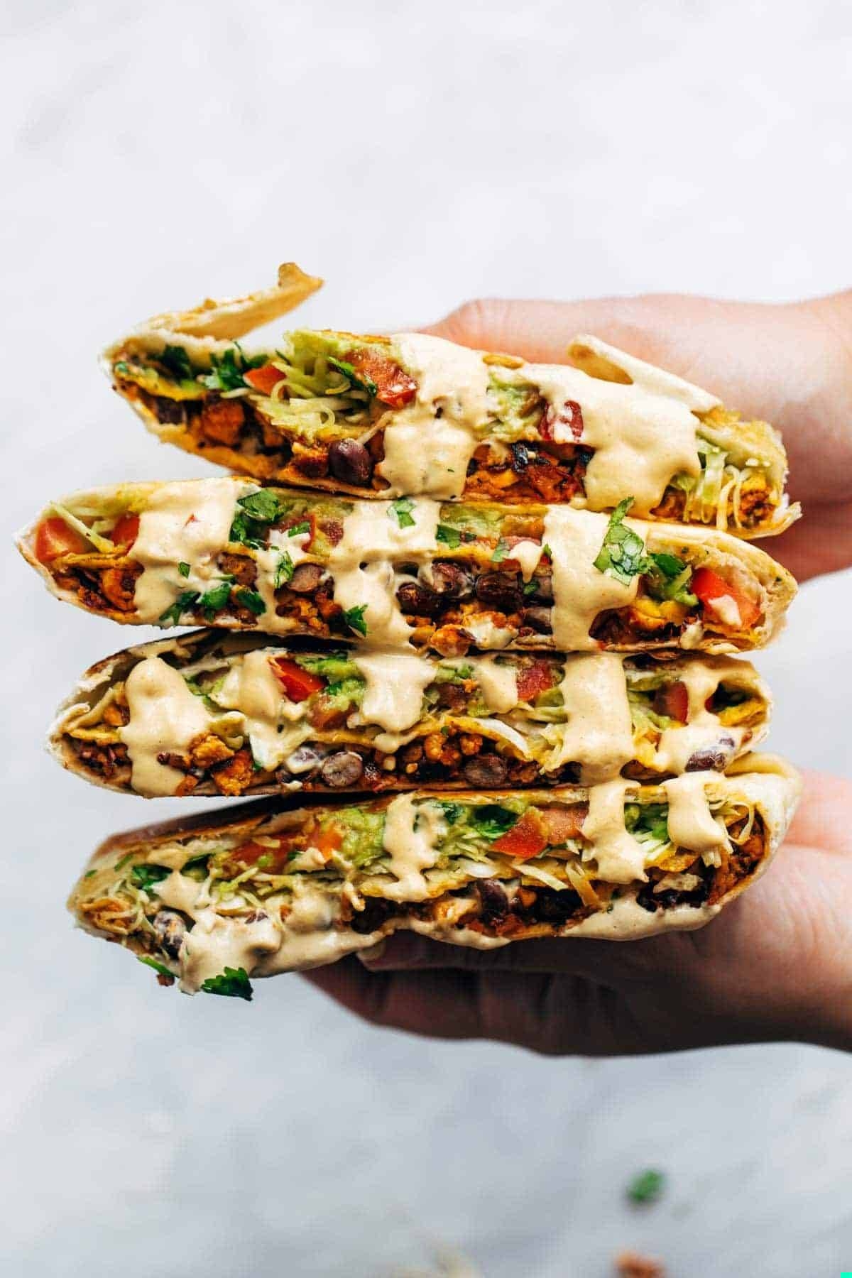 Hands holding stack pile of vegan crunchwrap.