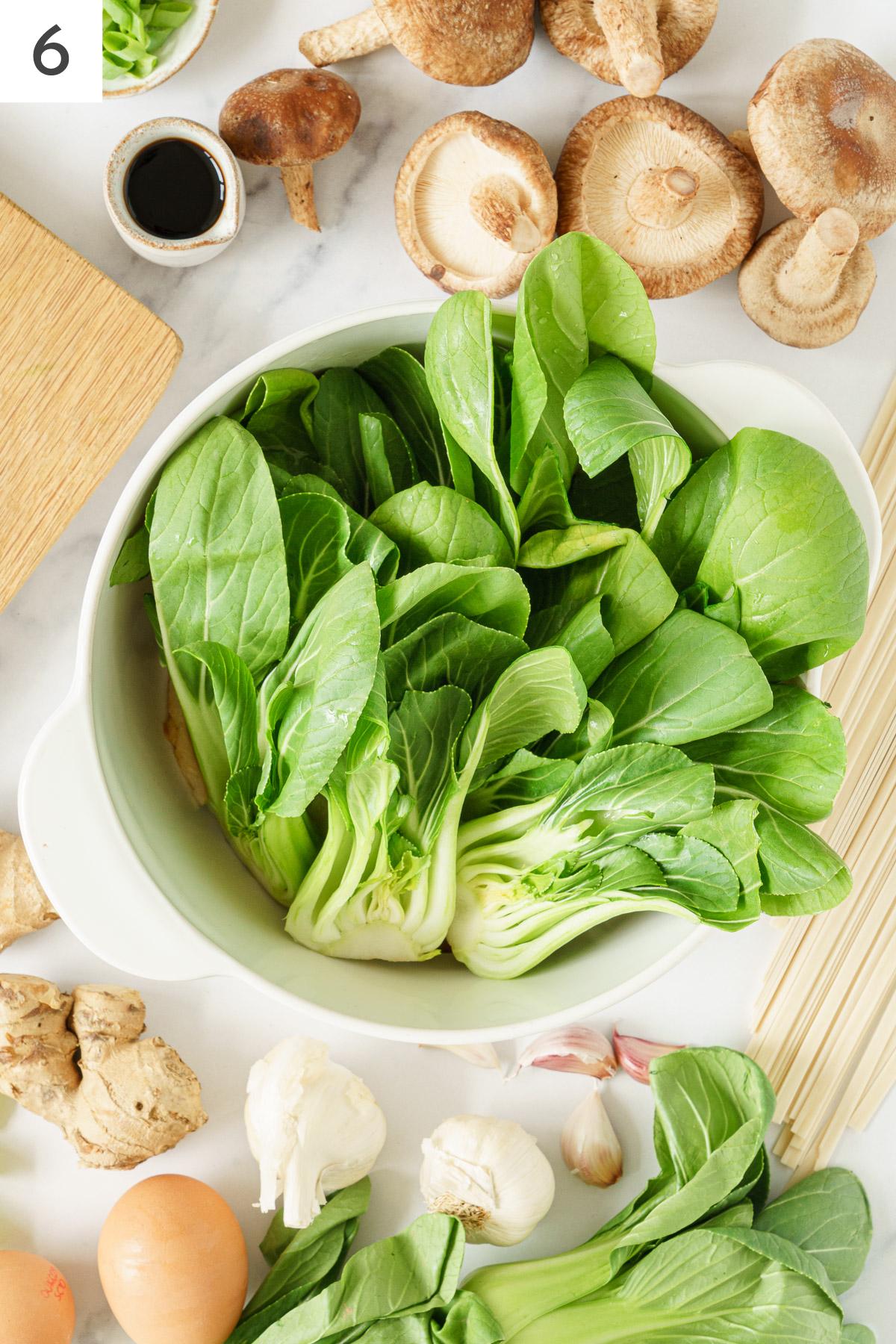 Bok choy added in to a pot with cooked mushrooms.