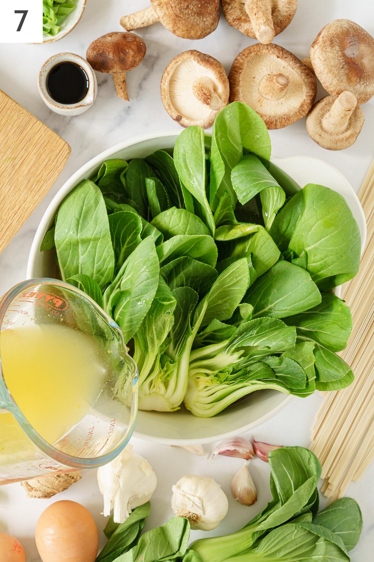 Broth poured into the pot with bok choy and cooked mushroms.