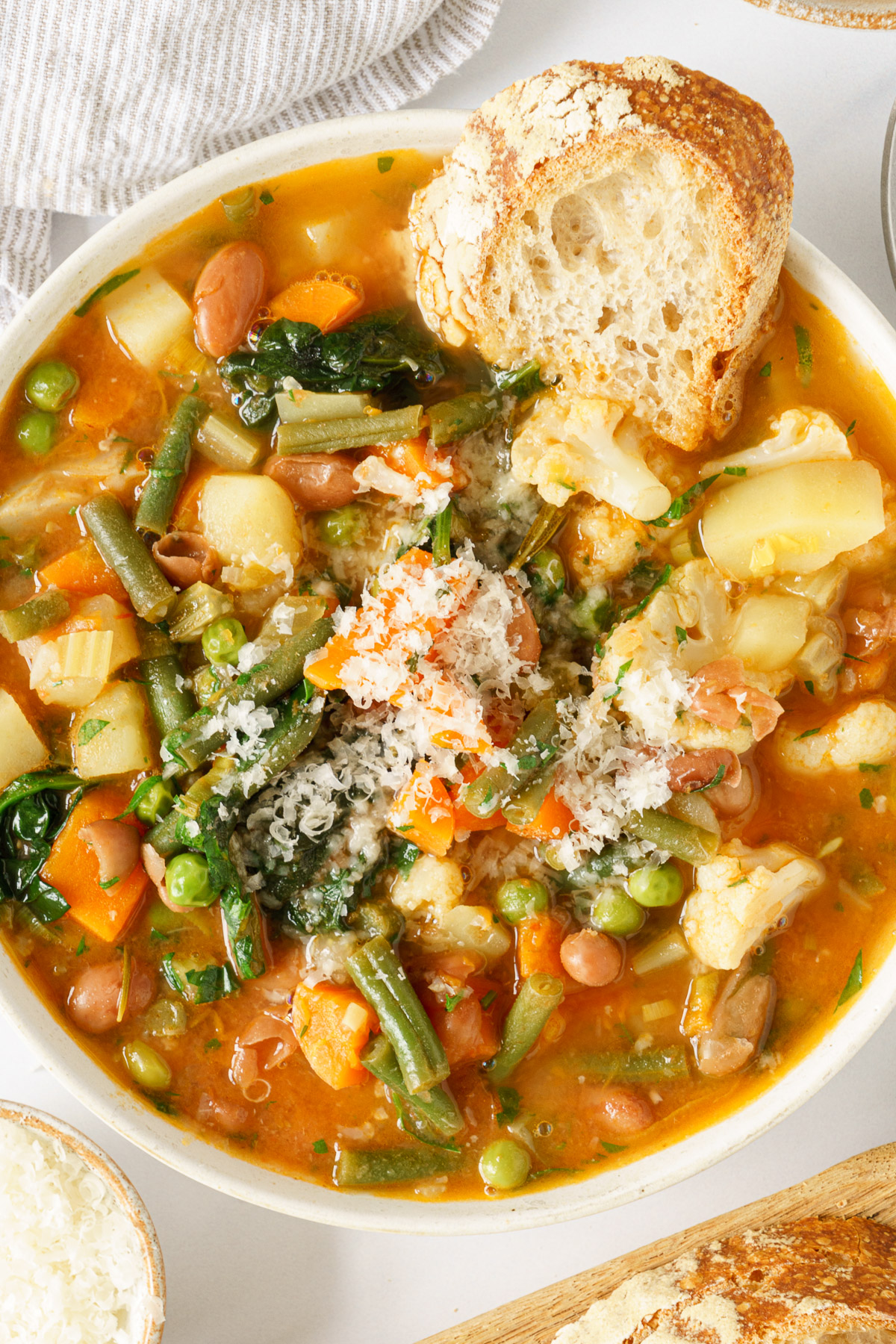 A bowl full of Italian minestrone soup topped with parmesan and bread.