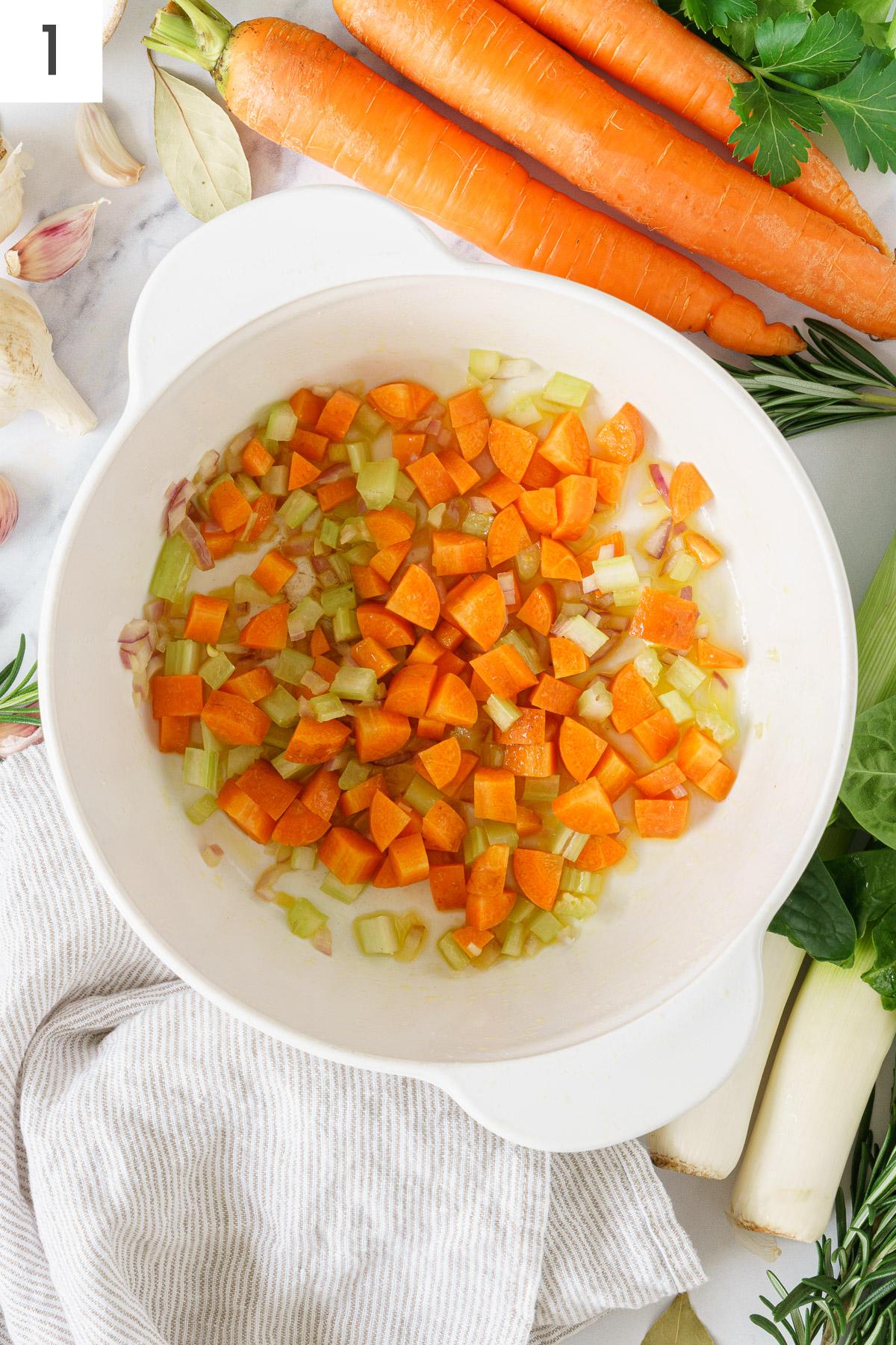 A cooking pot with cubes carots, chopped onion, celery and garlic.