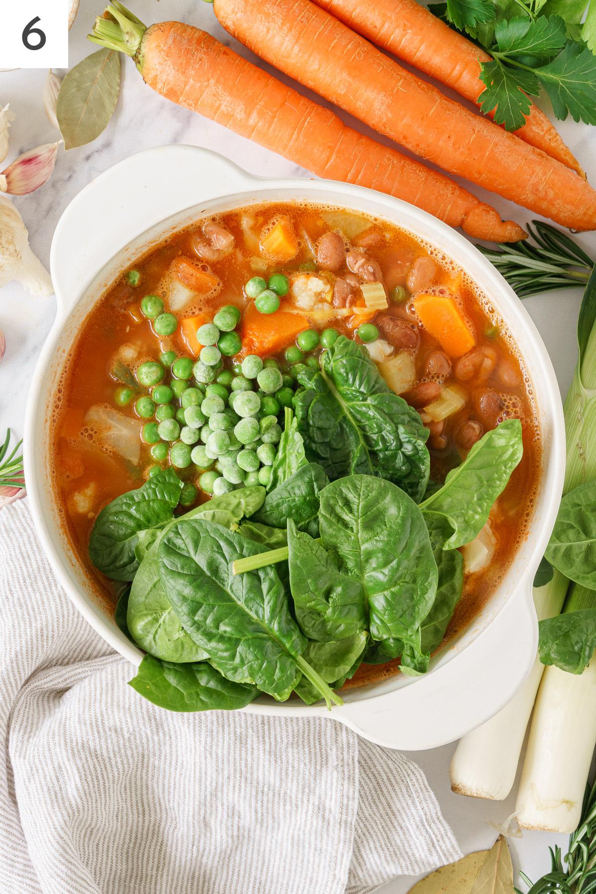 Cooking pot with Italian minestrone soup ingredients boiling with added green peas, and spinach.