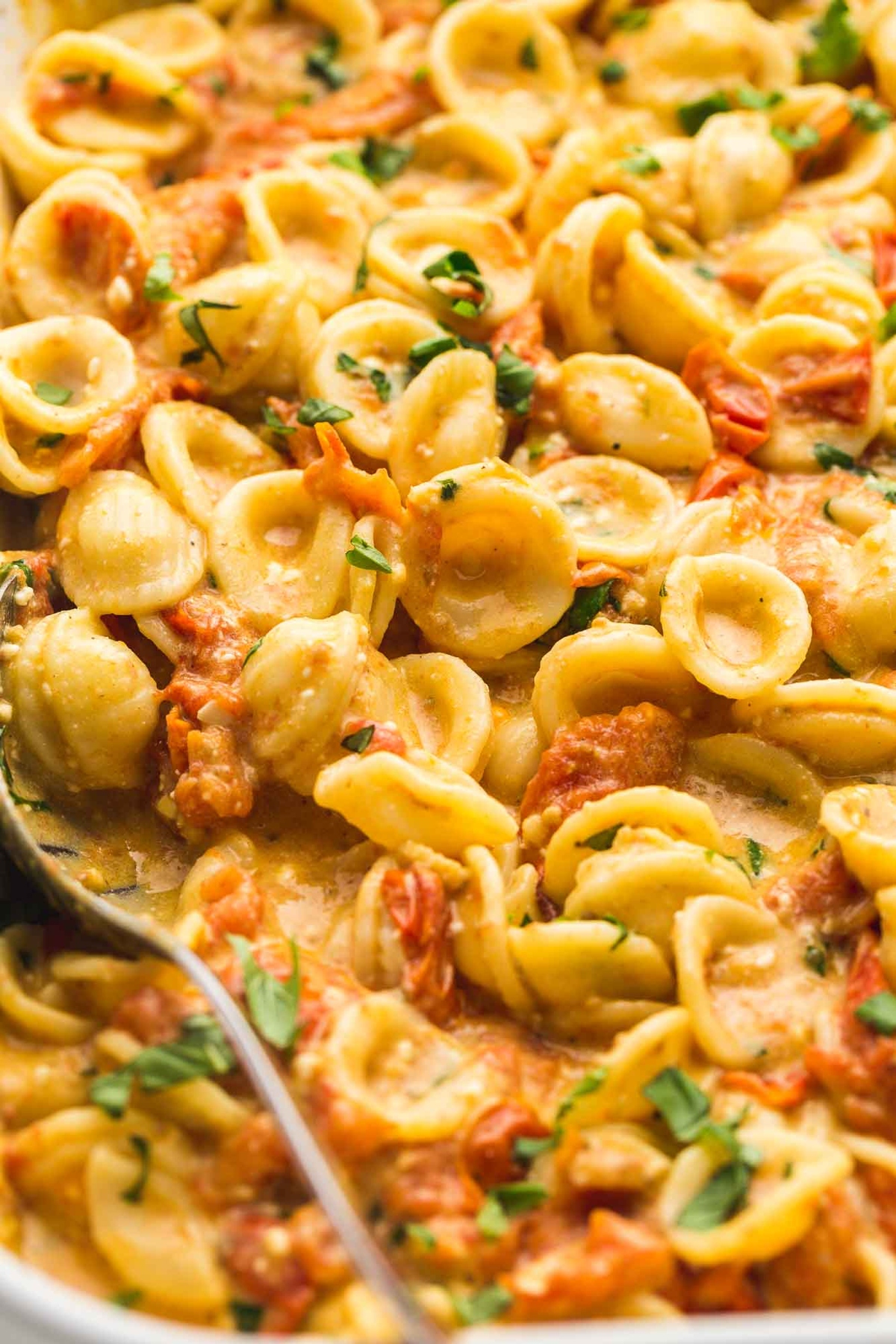 A spoon scoop a portion of baked feta pasta.