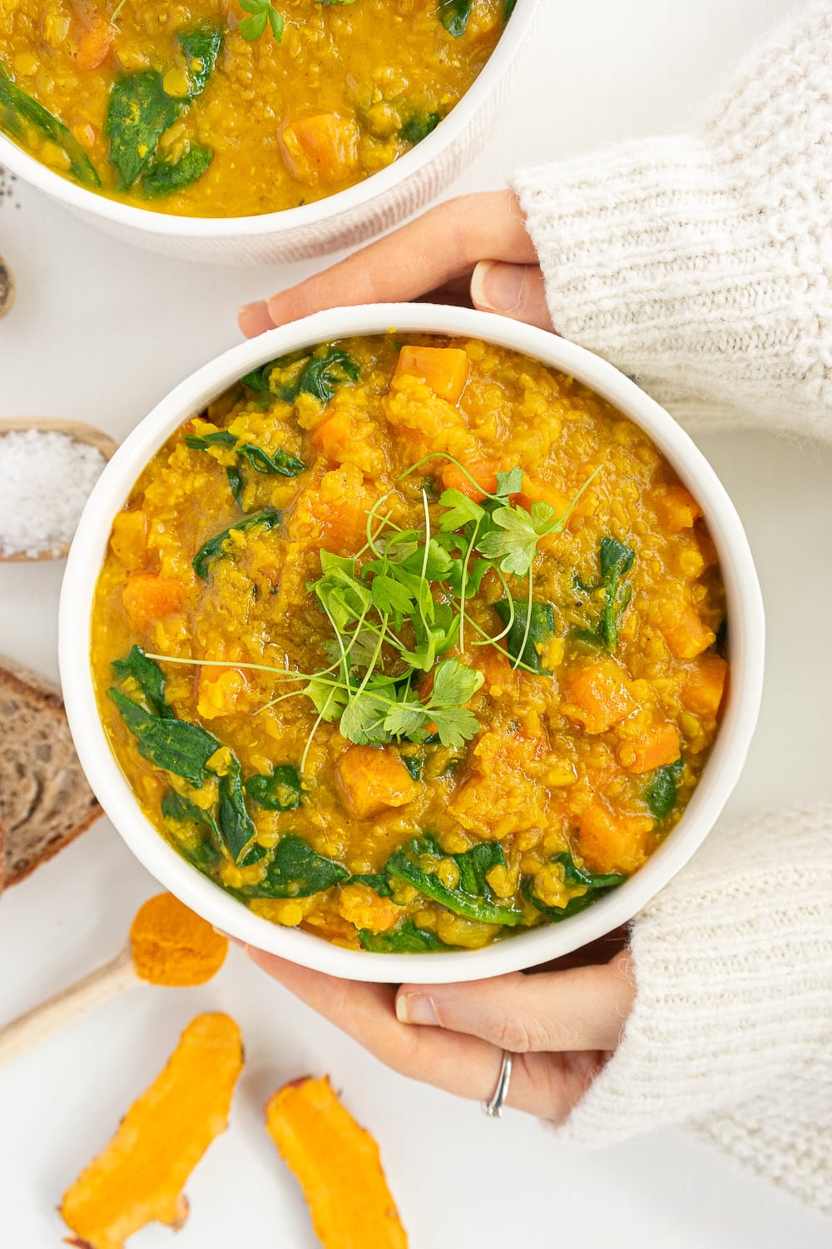 Hands holding a bowl of red lentil soup.