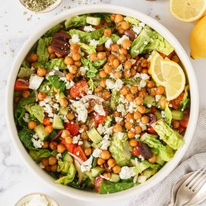 A bowl of roasted chickpea salad with mediterranean dressing drizzled with feta cheese.