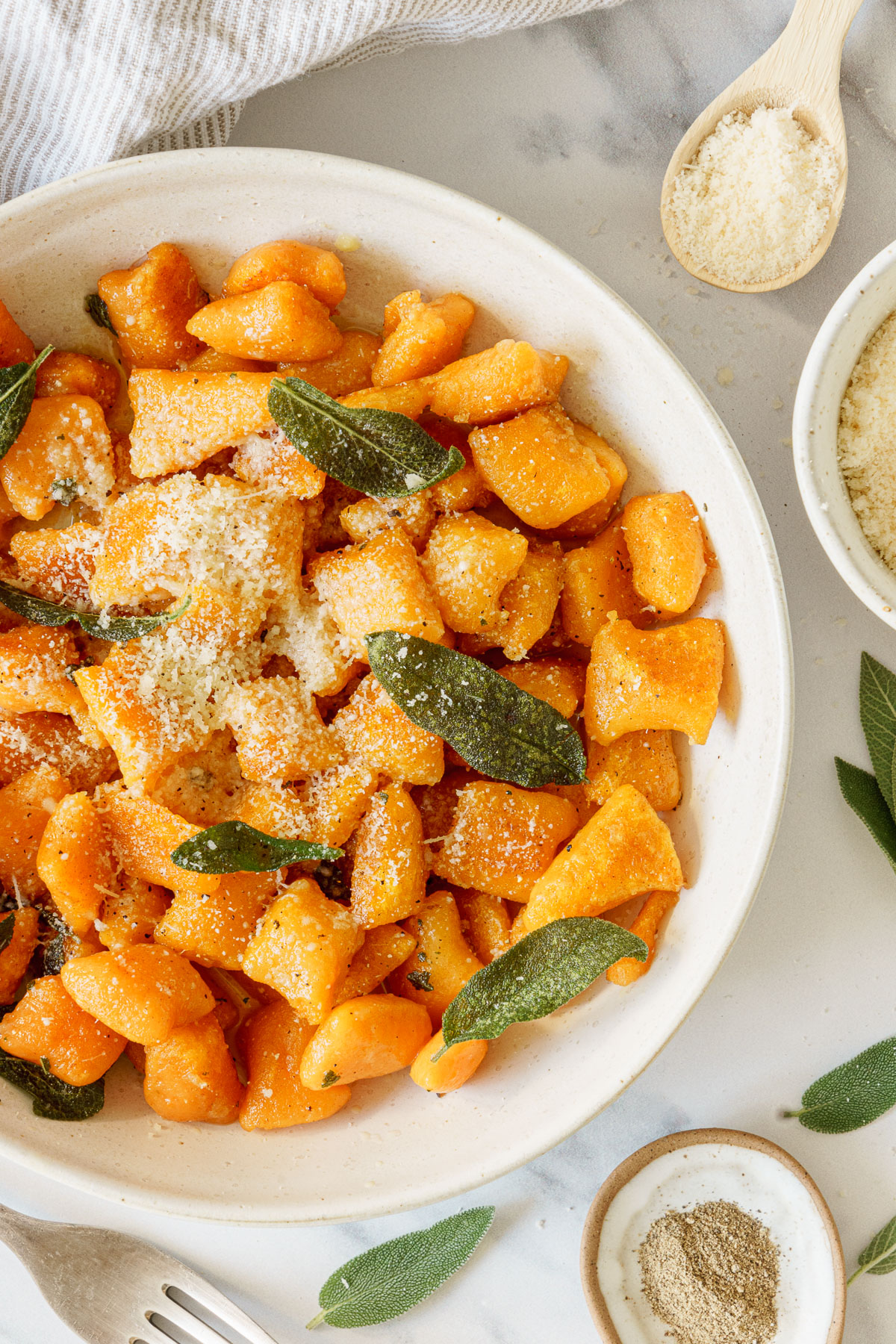 A plate of sweet potato gnocchi with parmesan cheese and sage leaves.